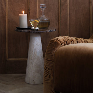 Small round table with a candle, glass, and decanter against a wooden paneled wall.